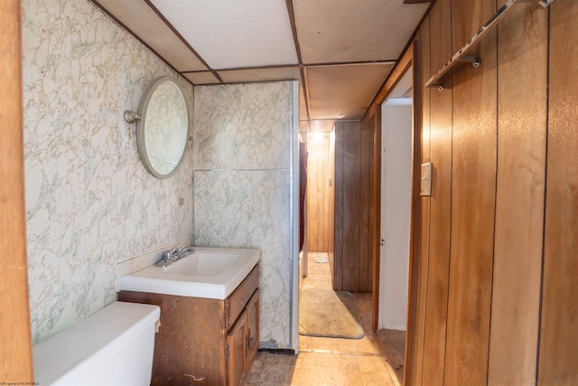 bathroom with tile patterned flooring, vanity, toilet, and a drop ceiling