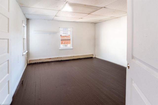 unfurnished room featuring dark wood-type flooring, a drop ceiling, and a baseboard heating unit