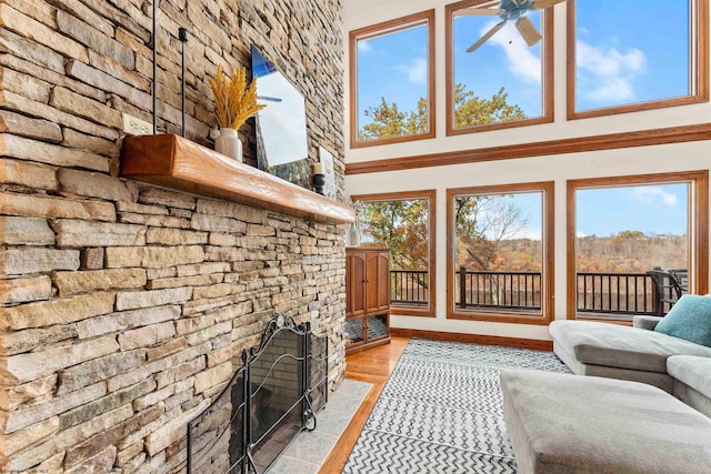 living room featuring a towering ceiling, a large fireplace, ceiling fan, and light wood-type flooring