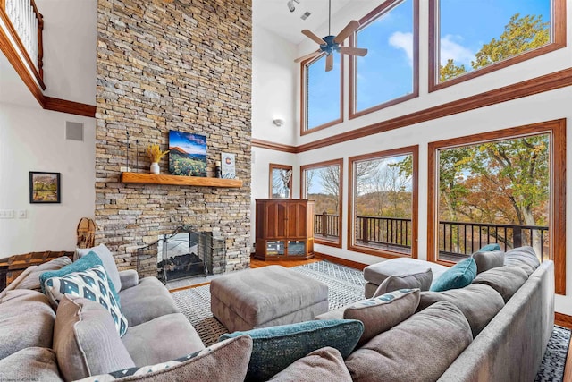 living room with hardwood / wood-style floors, a high ceiling, a stone fireplace, and ceiling fan