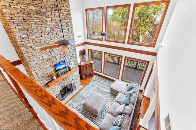 living room with a stone fireplace, light hardwood / wood-style flooring, ceiling fan, and a high ceiling