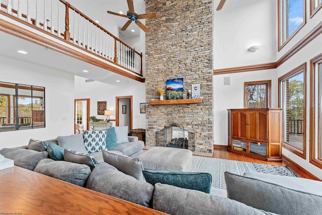 living room with a stone fireplace, light hardwood / wood-style floors, ceiling fan, and a high ceiling