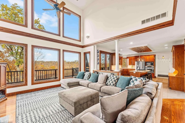 living room featuring a towering ceiling, ceiling fan, light hardwood / wood-style flooring, and decorative columns