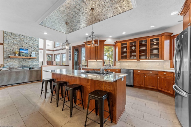 kitchen featuring light stone counters, stainless steel appliances, a breakfast bar, decorative columns, and a center island