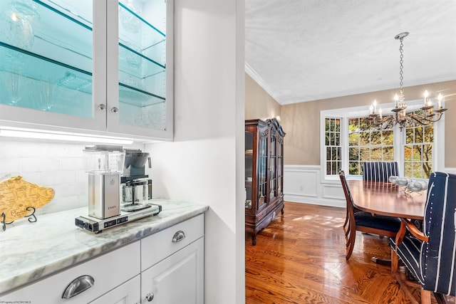 kitchen featuring ornamental molding, white cabinetry, light stone countertops, hanging light fixtures, and a chandelier