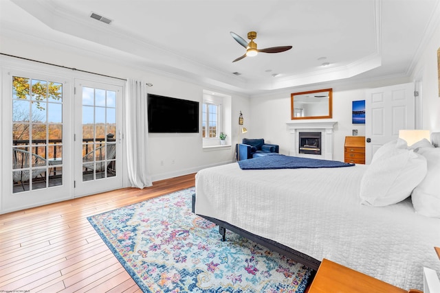 bedroom featuring ornamental molding, ceiling fan, access to exterior, wood-type flooring, and a raised ceiling