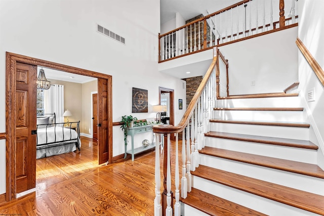 stairway with a towering ceiling, wood-type flooring, and a chandelier