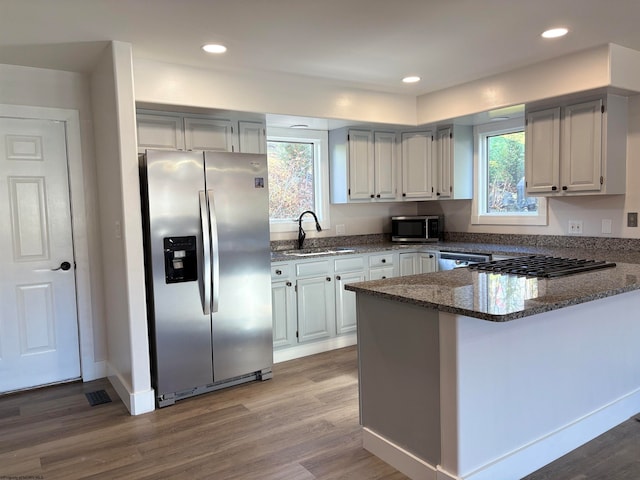 kitchen featuring wood-type flooring, kitchen peninsula, sink, appliances with stainless steel finishes, and dark stone countertops