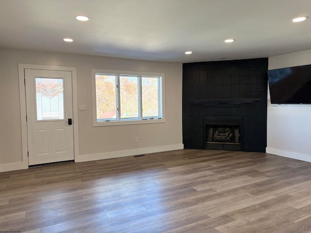 unfurnished living room featuring wood-type flooring and a tile fireplace