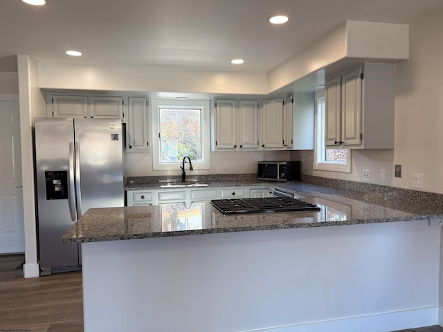 kitchen with sink, kitchen peninsula, appliances with stainless steel finishes, dark stone counters, and dark wood-type flooring