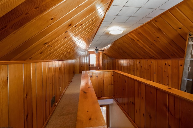 corridor with wood walls, light carpet, and vaulted ceiling