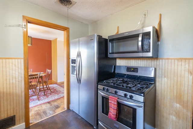 kitchen featuring stainless steel appliances, dark wood-type flooring, a textured ceiling, and wooden walls