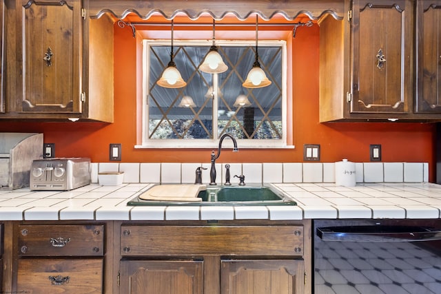 kitchen featuring dishwasher, sink, pendant lighting, and tile counters