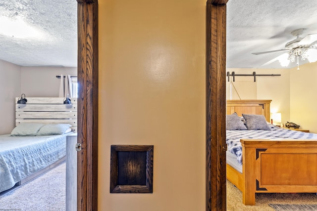 bedroom with a barn door, ceiling fan, a textured ceiling, and light carpet