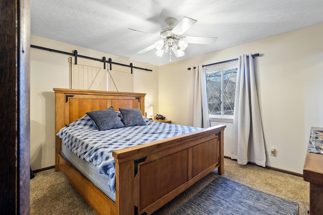 carpeted bedroom with a barn door, ceiling fan, and a textured ceiling