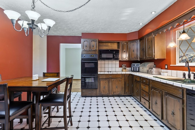 kitchen featuring tile counters, dark brown cabinetry, black appliances, sink, and decorative light fixtures