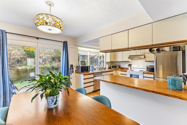 kitchen featuring appliances with stainless steel finishes, decorative light fixtures, white cabinets, light hardwood / wood-style floors, and butcher block counters