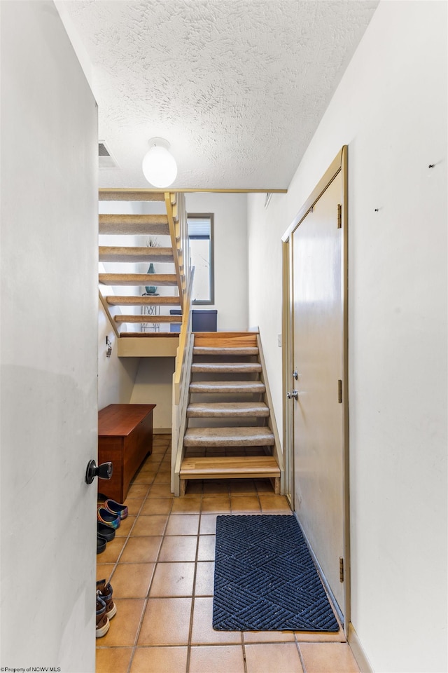 staircase with a textured ceiling and tile patterned floors