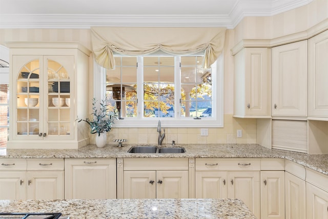 kitchen featuring ornamental molding, sink, decorative backsplash, cream cabinetry, and light stone countertops