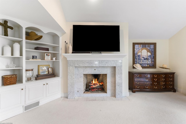 living room featuring a tiled fireplace, built in shelves, light colored carpet, and lofted ceiling