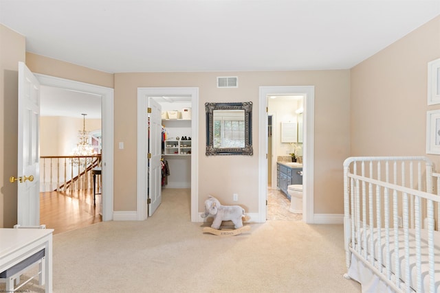 carpeted bedroom with connected bathroom, a chandelier, and a nursery area