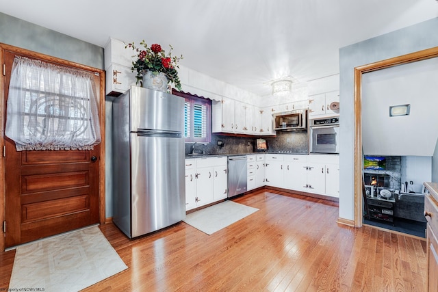 kitchen featuring white cabinetry, sink, appliances with stainless steel finishes, light hardwood / wood-style floors, and backsplash