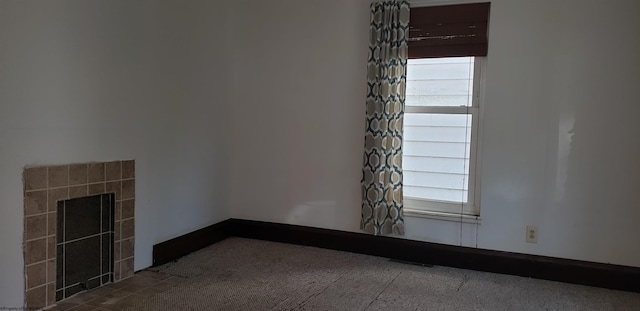 unfurnished room with a fireplace, dark colored carpet, and plenty of natural light