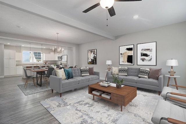 living room with light wood-type flooring, ceiling fan with notable chandelier, beamed ceiling, and sink