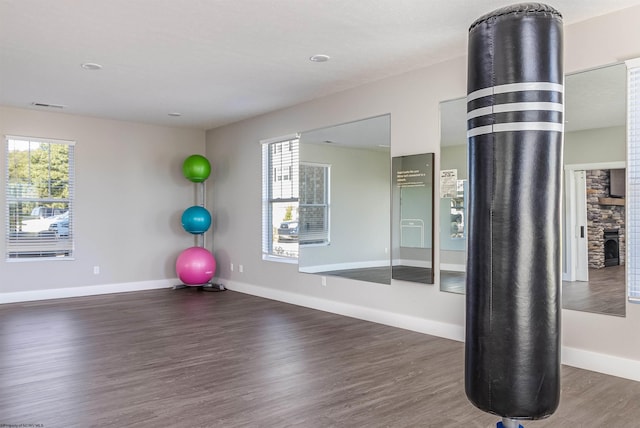 workout room with a stone fireplace and dark wood-type flooring