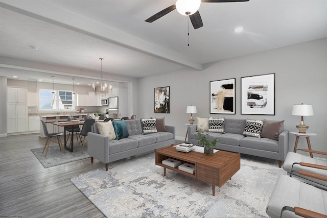 living room with beam ceiling, sink, light hardwood / wood-style floors, and ceiling fan with notable chandelier