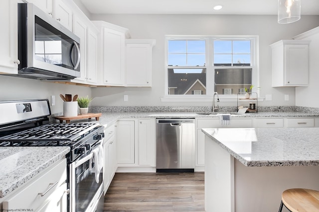 kitchen with appliances with stainless steel finishes, hardwood / wood-style flooring, white cabinetry, and a kitchen breakfast bar