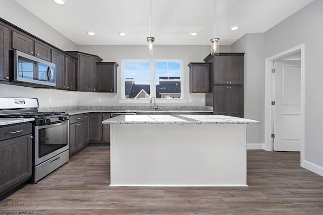 kitchen with dark hardwood / wood-style flooring, decorative light fixtures, dark brown cabinets, a kitchen island, and appliances with stainless steel finishes