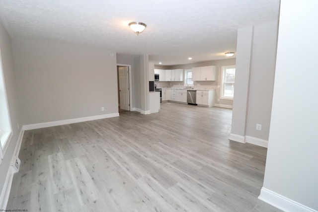 unfurnished living room with light hardwood / wood-style floors, sink, and a textured ceiling