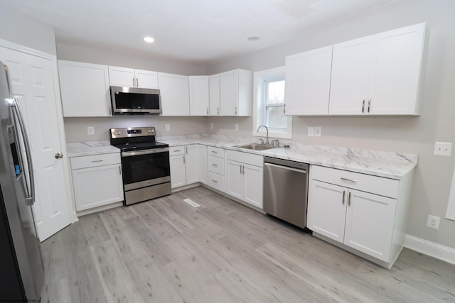 kitchen with white cabinets, sink, light hardwood / wood-style flooring, light stone countertops, and appliances with stainless steel finishes