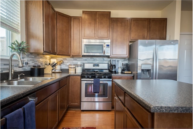 kitchen with a center island, backsplash, sink, light wood-type flooring, and stainless steel appliances