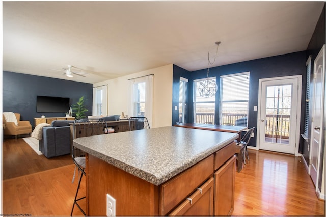 kitchen with ceiling fan, hanging light fixtures, light hardwood / wood-style floors, a breakfast bar area, and a kitchen island