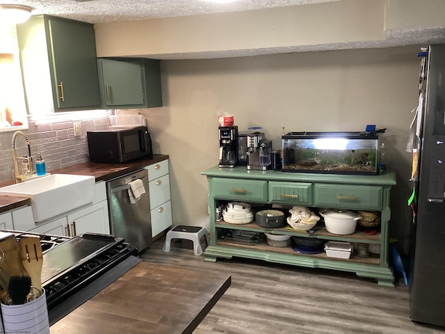 kitchen featuring green cabinets, dark wood-type flooring, stainless steel dishwasher, and sink