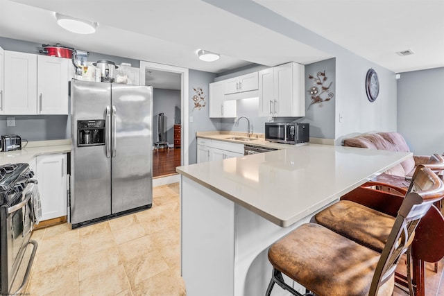 kitchen featuring kitchen peninsula, appliances with stainless steel finishes, sink, white cabinets, and a breakfast bar area