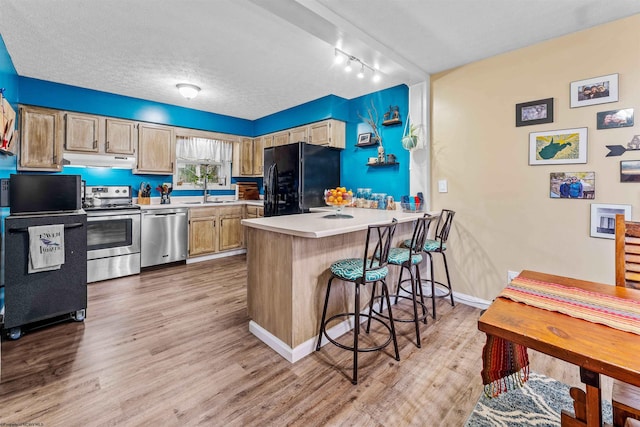 kitchen featuring track lighting, light hardwood / wood-style flooring, appliances with stainless steel finishes, a kitchen bar, and kitchen peninsula