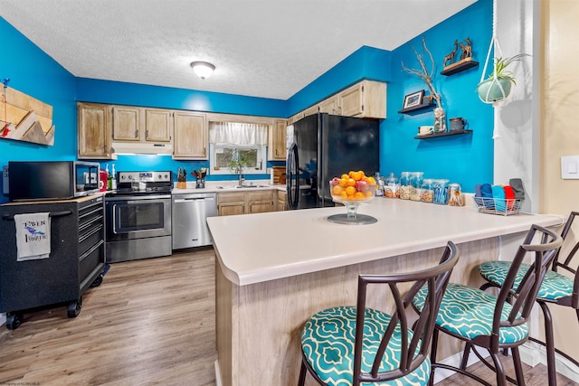 kitchen featuring a kitchen breakfast bar, light wood-type flooring, a textured ceiling, appliances with stainless steel finishes, and kitchen peninsula