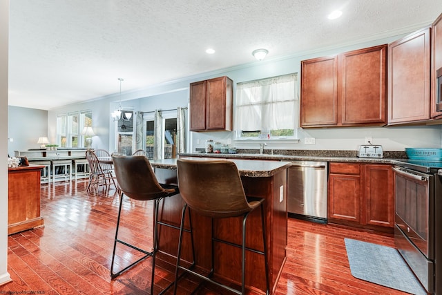 kitchen with pendant lighting, stainless steel appliances, a kitchen bar, and dark wood-type flooring