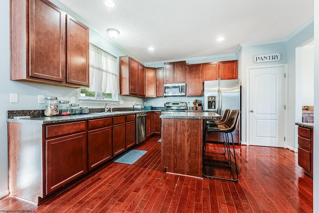 kitchen featuring a breakfast bar, ornamental molding, dark hardwood / wood-style floors, a kitchen island, and stainless steel appliances