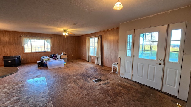 entryway with ceiling fan, a textured ceiling, and wooden walls