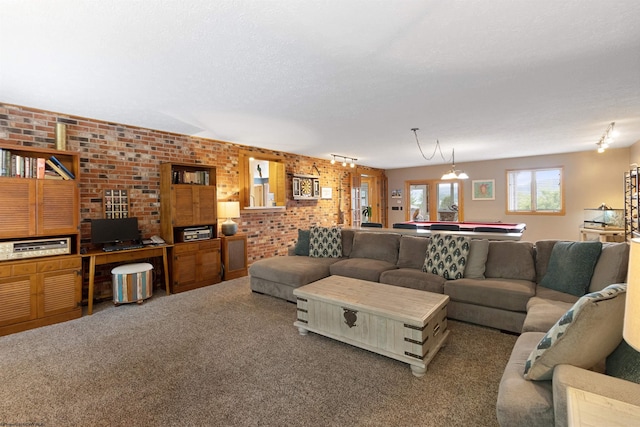 living room featuring a chandelier, carpet floors, brick wall, and rail lighting