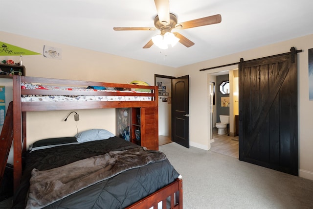 carpeted bedroom with a barn door, ensuite bath, and ceiling fan