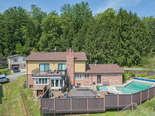 rear view of property featuring a lawn, a balcony, and a pool side deck