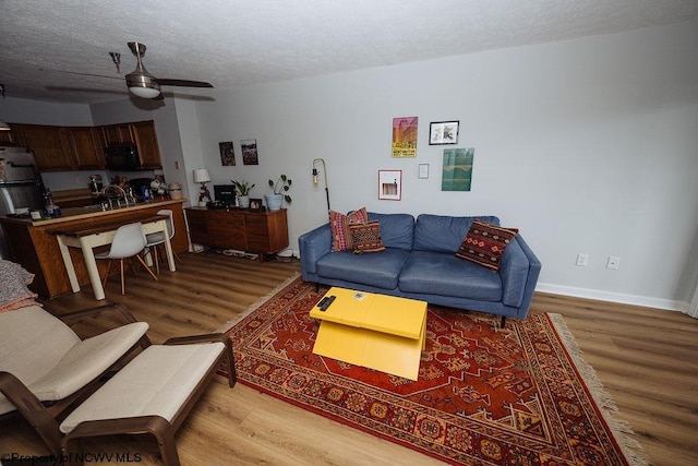 living room with ceiling fan, a textured ceiling, and light wood-type flooring