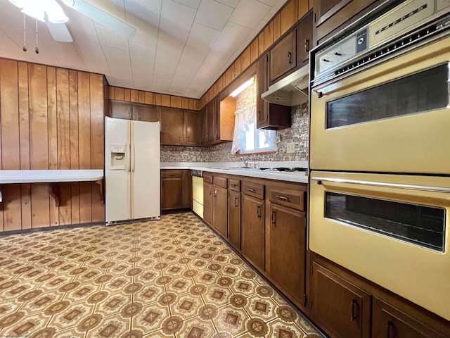 kitchen featuring white appliances, ceiling fan, wood walls, and backsplash