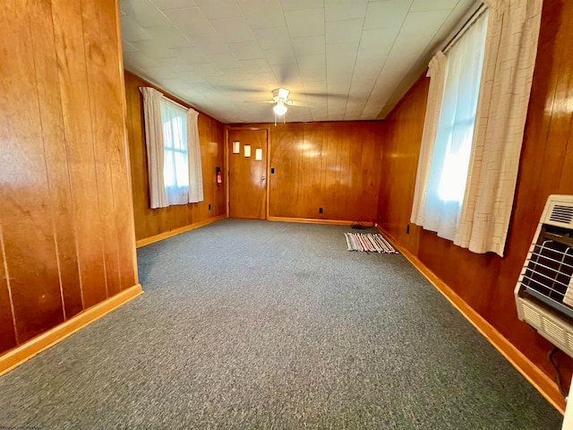 empty room with ceiling fan, dark carpet, wooden walls, and heating unit