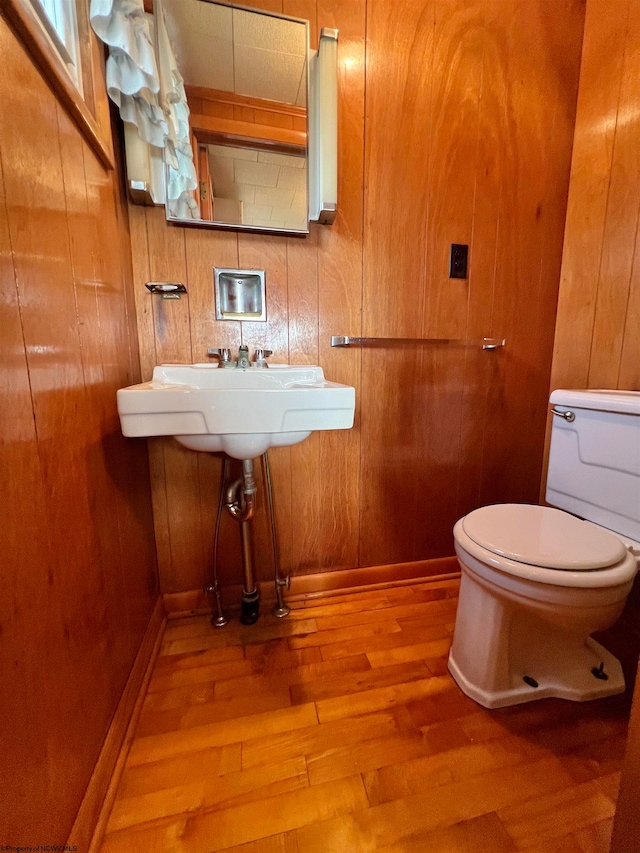 bathroom featuring hardwood / wood-style floors, toilet, sink, and wooden walls